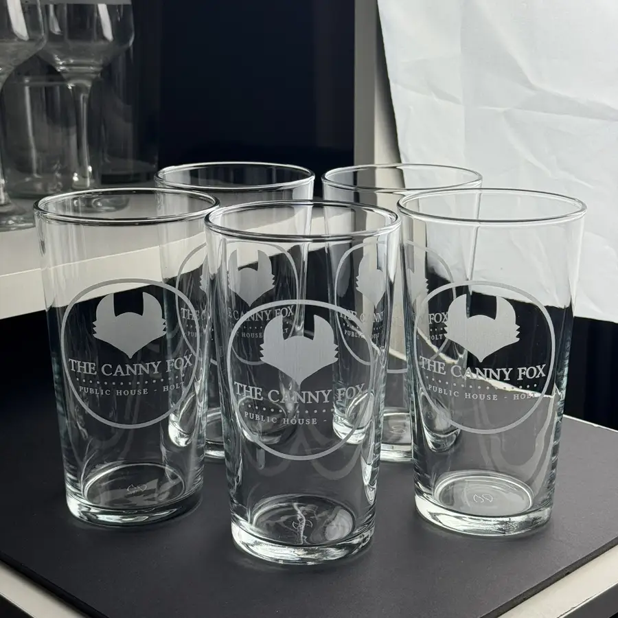 Five conical pints engraved with a pub’s logo, lined up on the bar