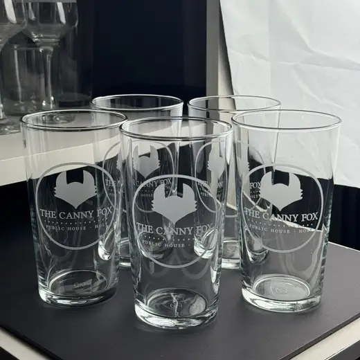 Five conical pints engraved with a pub’s logo, lined up on the bar