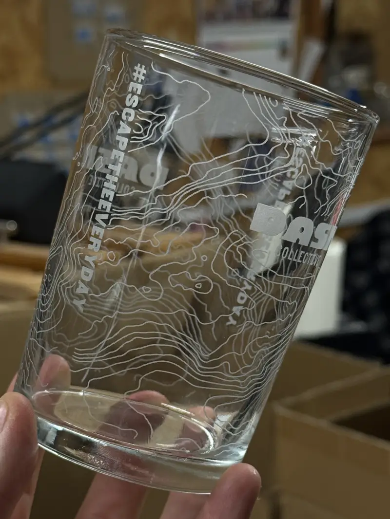 A pint glass engraved with contour lines wrapping the full circumference